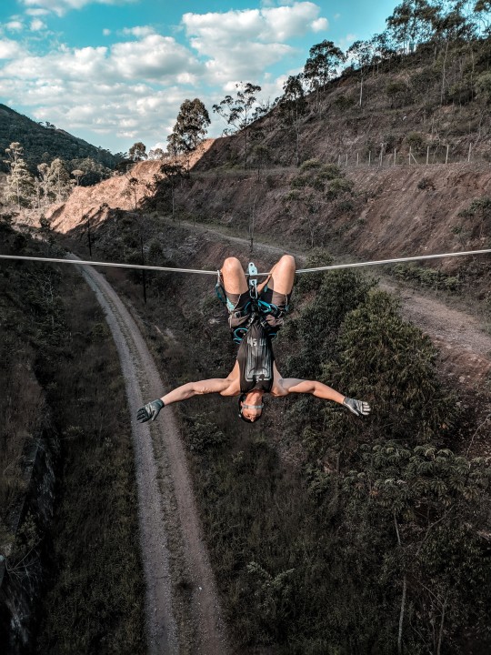 Man hanging over a horizontal wire under his knees over valley.