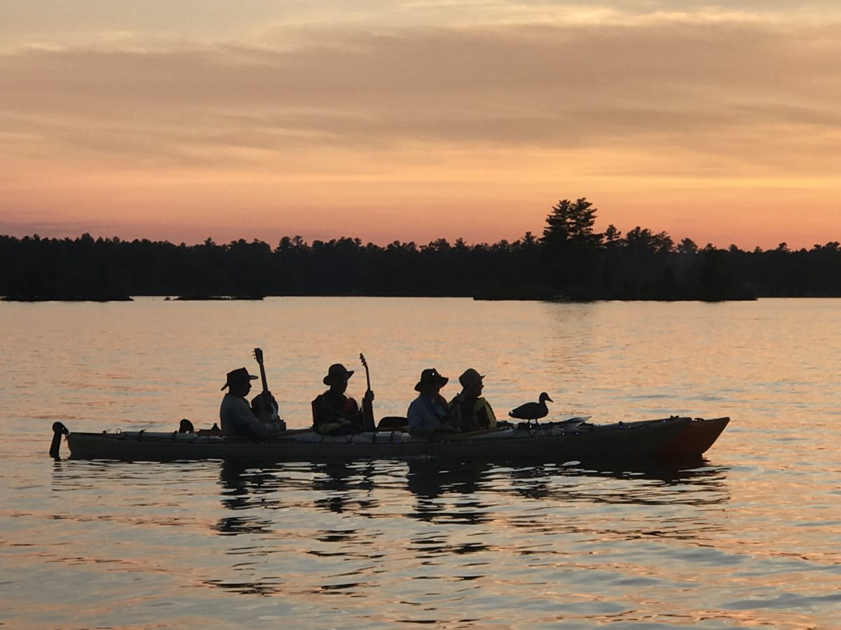People with musical instruments in a canoes at sunset
