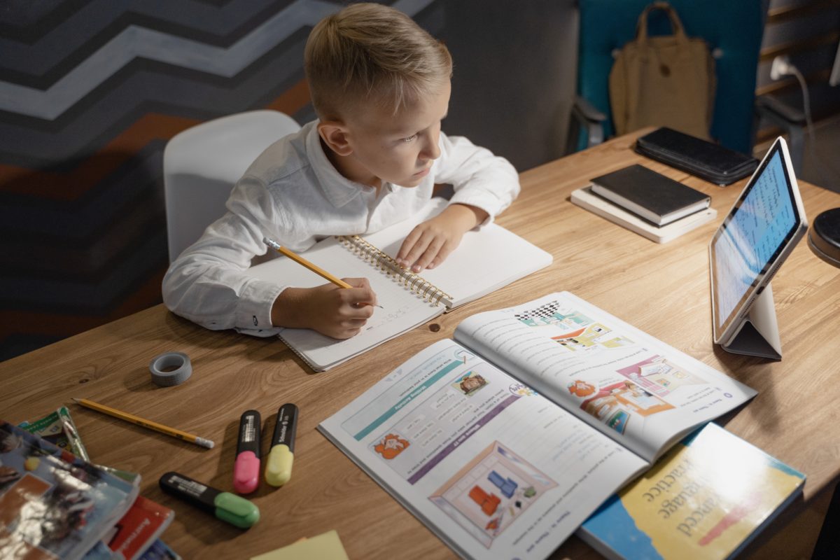 Young child working at his desk surrounded by books and a monitor.