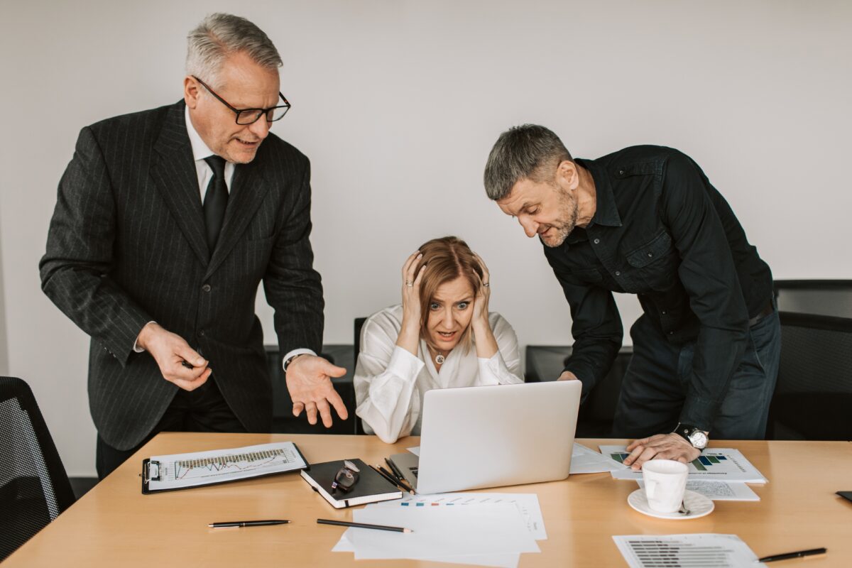 Two men in suits standing over a woman at a computer.