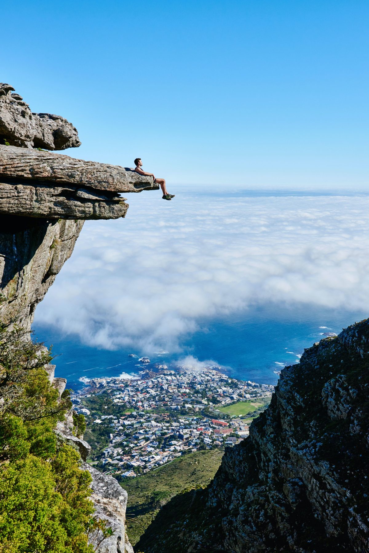 Person sitting on a mountain cliff overlooking a city.
