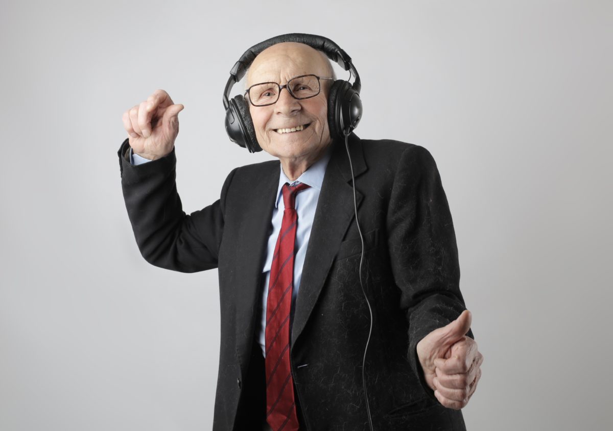 Elderly man in a suit wearing headphones and dancing.