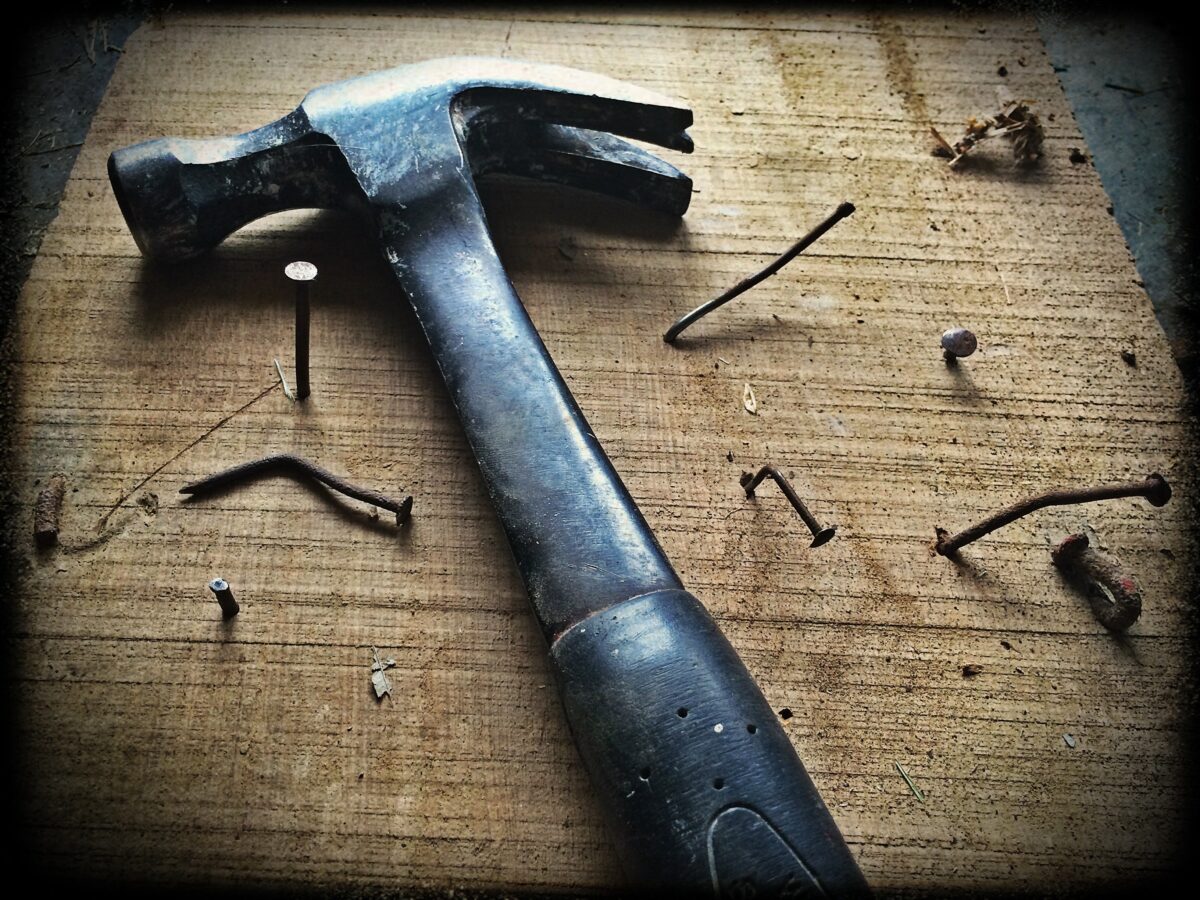 A hammer on a board with various nails around it.