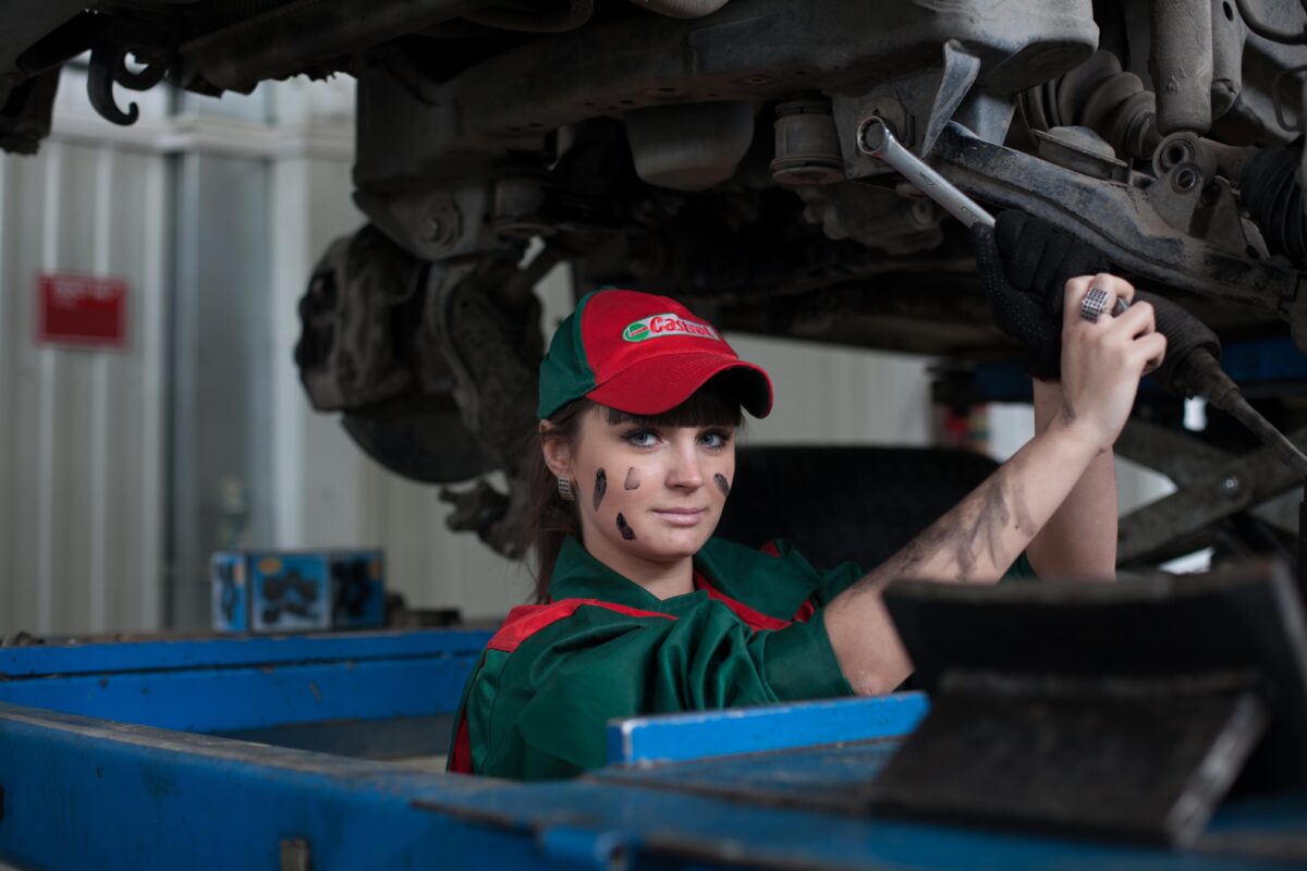 Woman working in garage, standing in bay fixing a car.