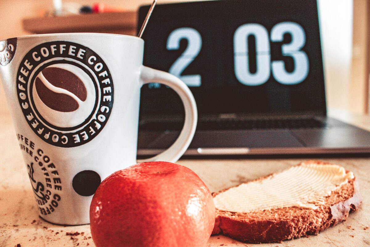 An apple, a coffee cup, a slice of bread with butter and a clock showing 2:03 pm, all suggesting someone eating while they work.