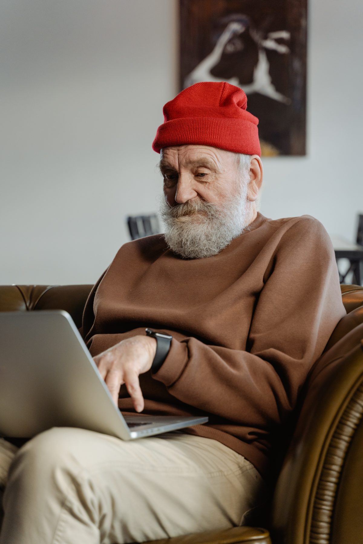 Older man with white beard wearing a red hat using his computer.