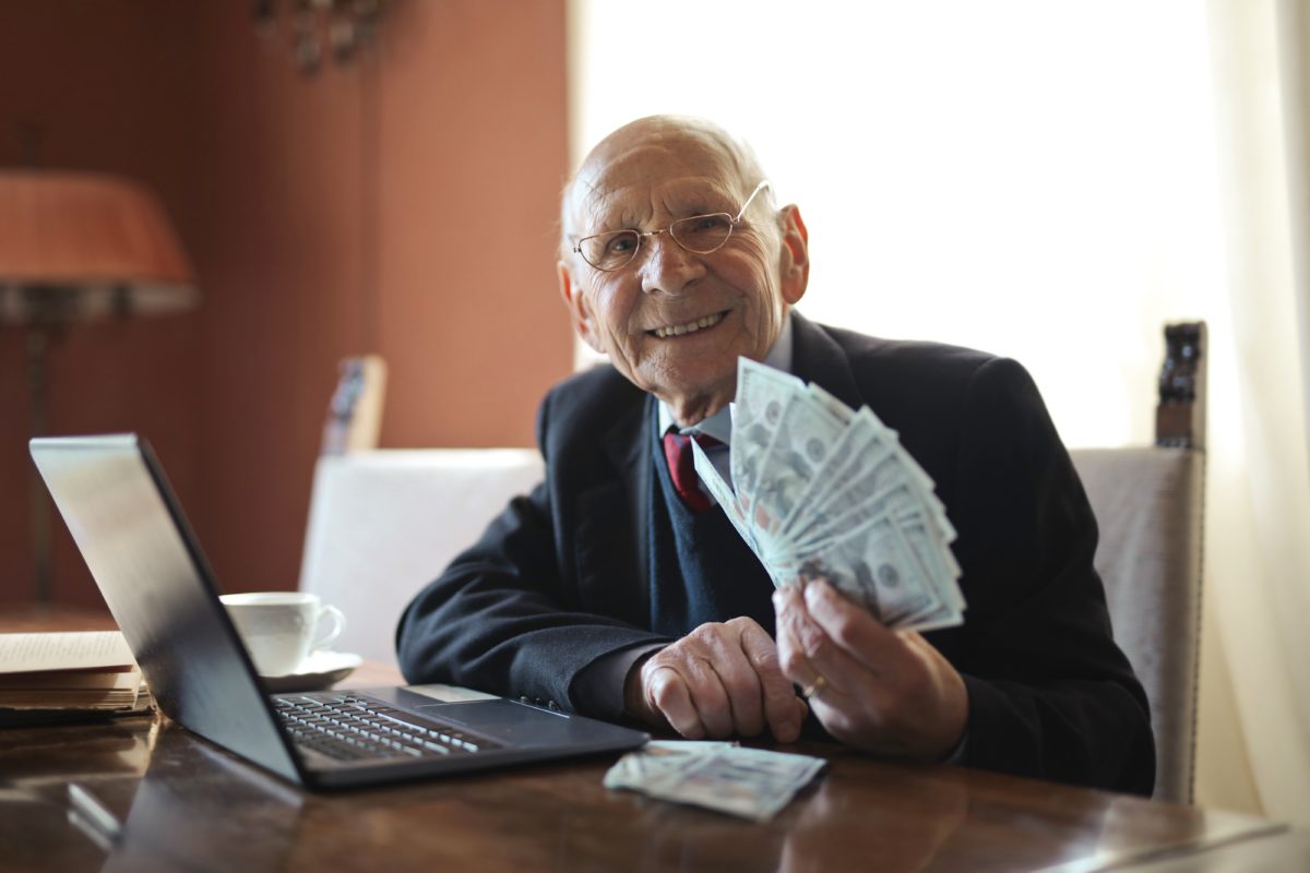 Man in suit at desk with computer and holding dollar bills.