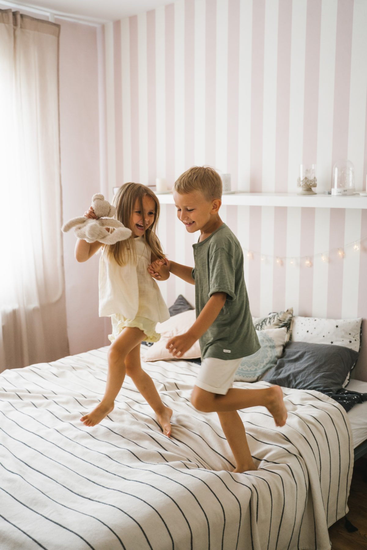 Young girl and boy jumping on a bed.