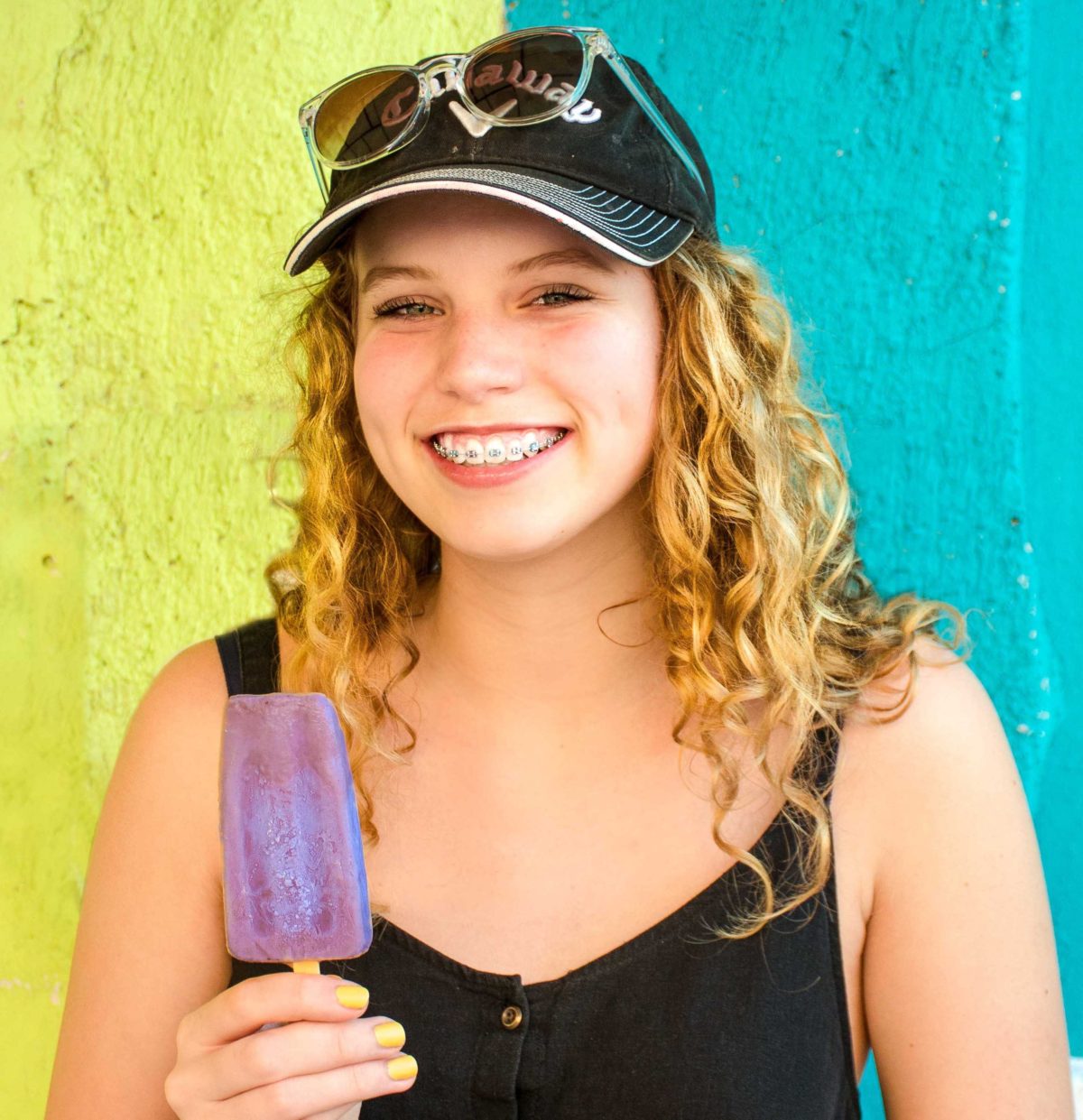 Young woman smiling and eating a grape popsicle.