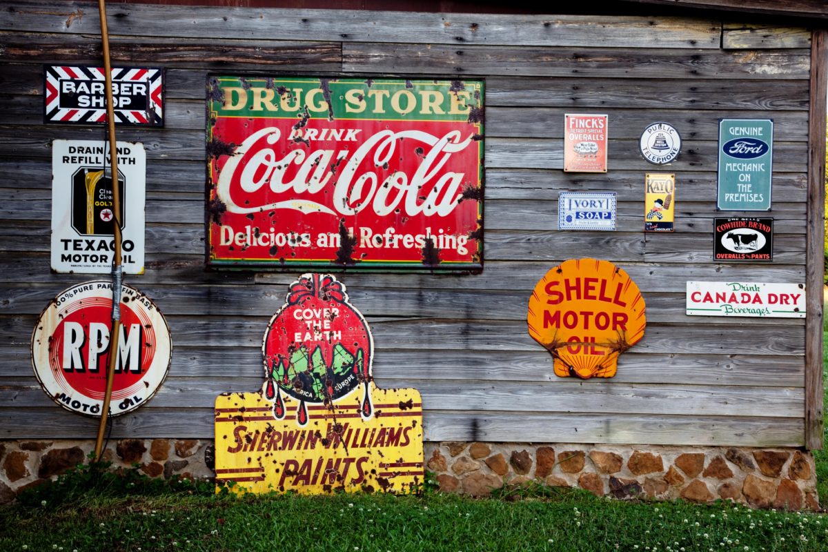 A wall with vintage advertising signs on it including Coca-Cola, Sherwin Williams and Shell Oil.