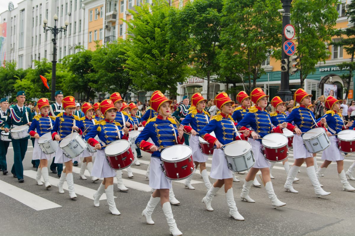 Marching band of female musicians wearing blue and white uniforms and playing drums.