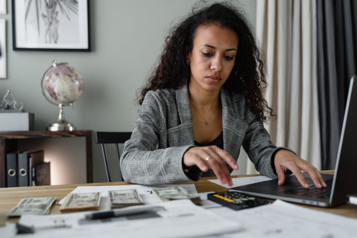 Woman working with calculator and computer, with dollar bills on her desk.