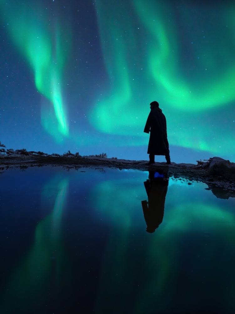 Silhouette of a man walking under the Northern LIghts.