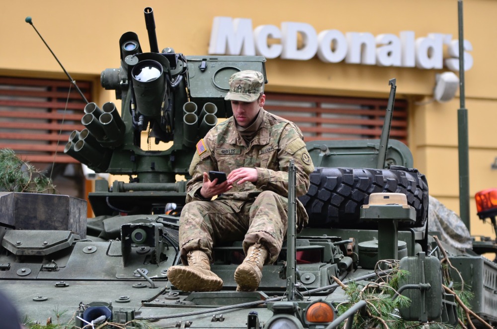 Soldier sitting on tank outside of McDonald's, using cell phone.