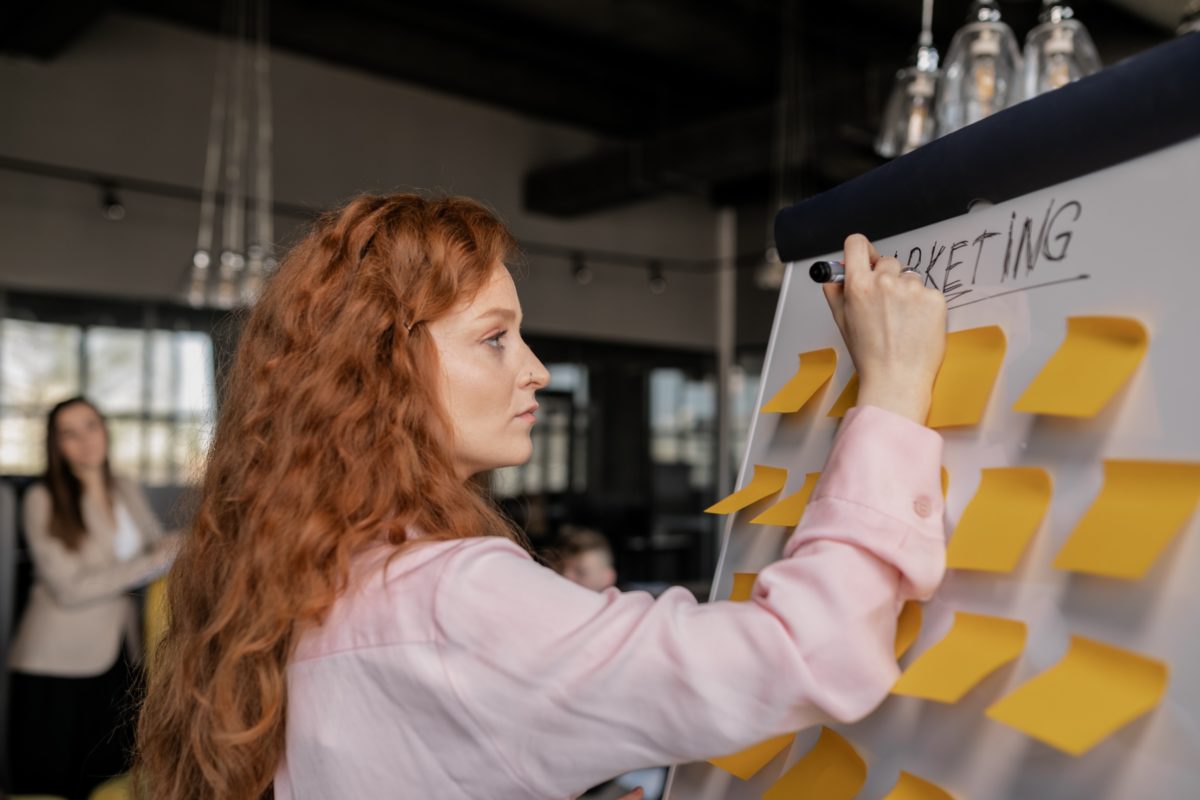 Woman standing at whiteboard that says "Marketing" and has numerous sticky notes.