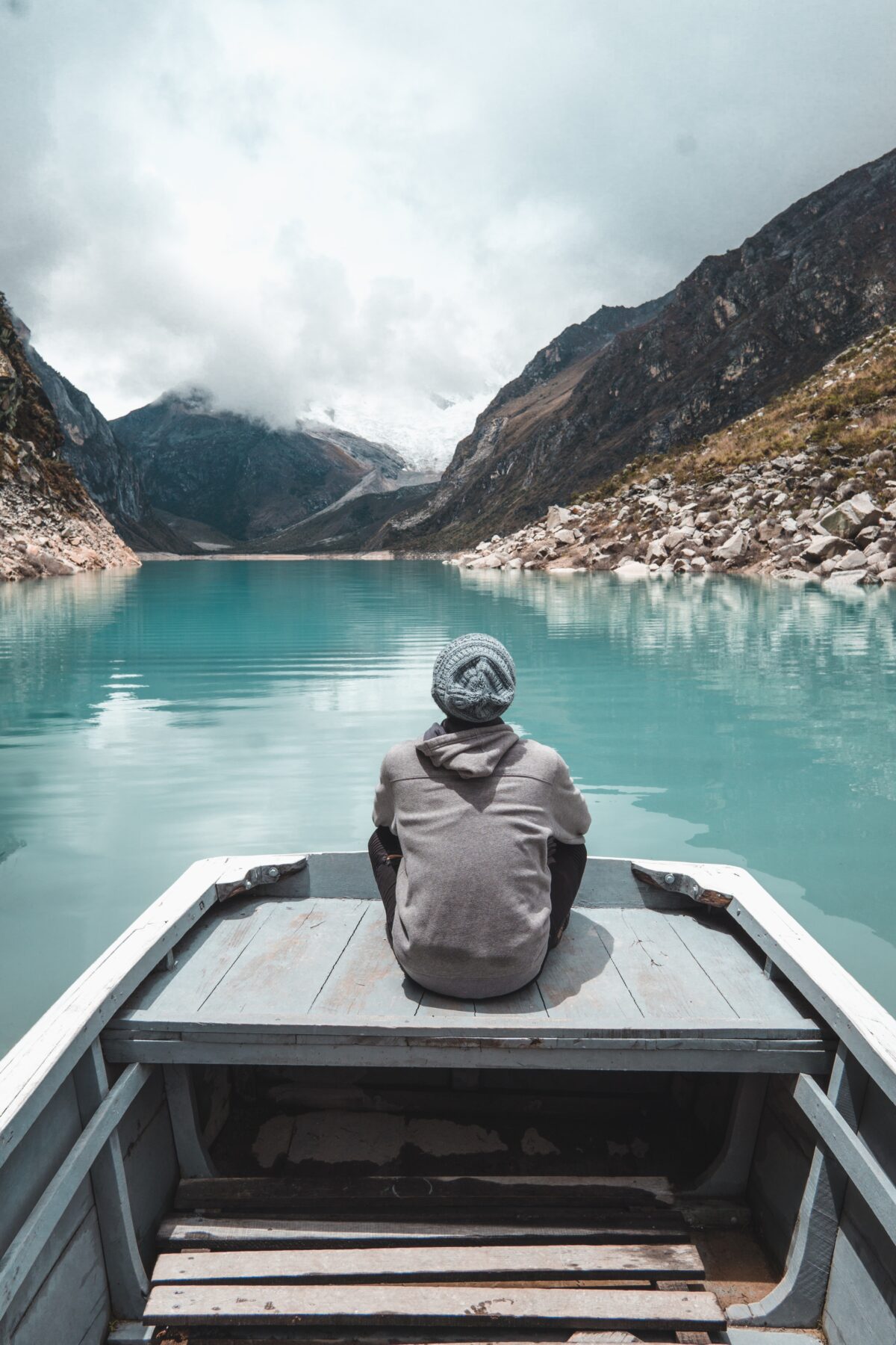 A person sitting in the stern of a small boat facing away from the camera with mountains ahead of them.