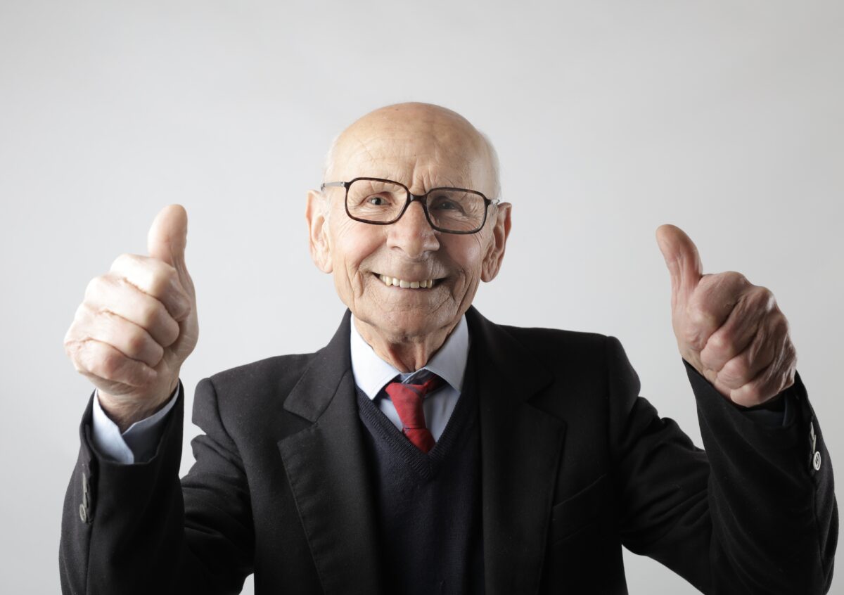 Older man smiling and giving thumbs up sign.