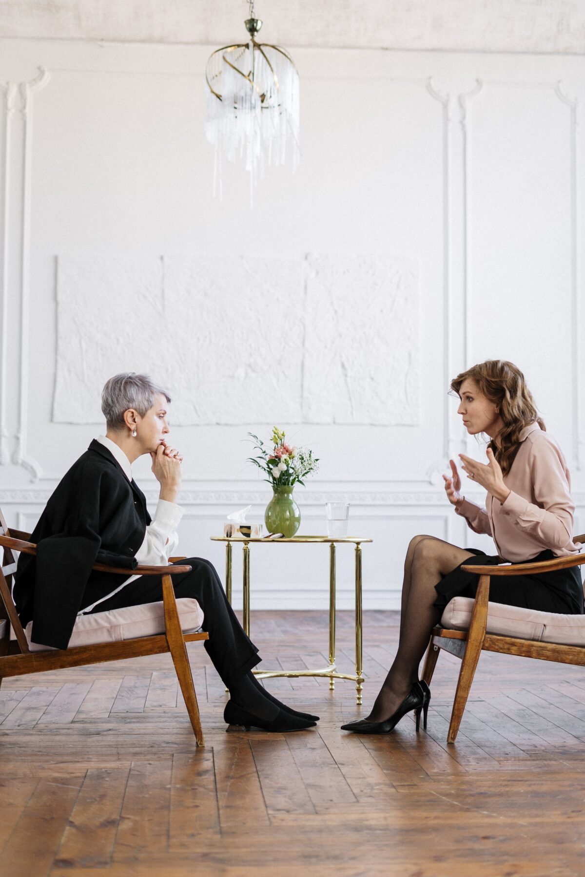 Two women sitting across from each other on brown chairs talking to each other.