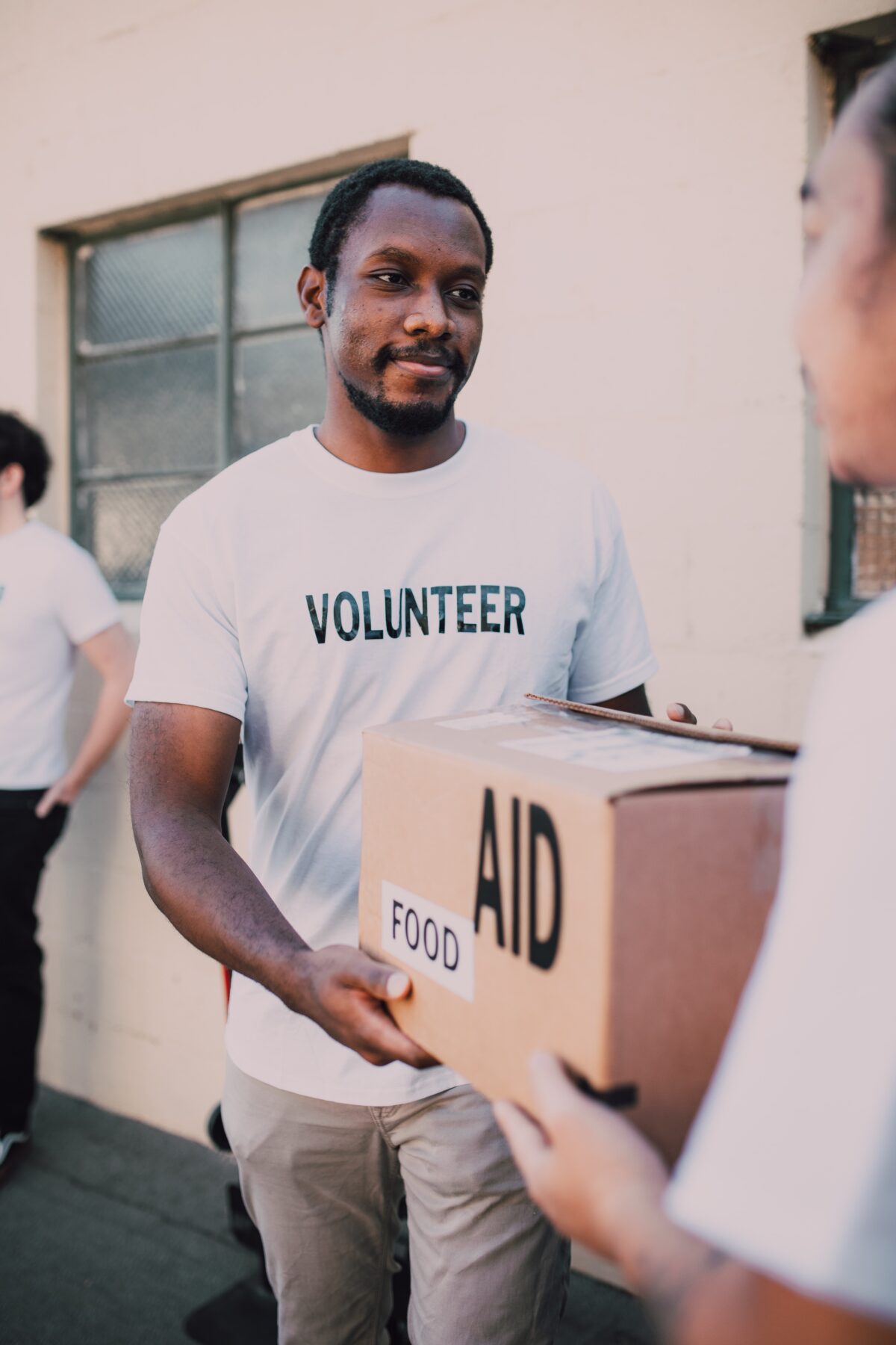 Man holding box marked "Aid" and wearing a tee shirt which says "Volunteer."