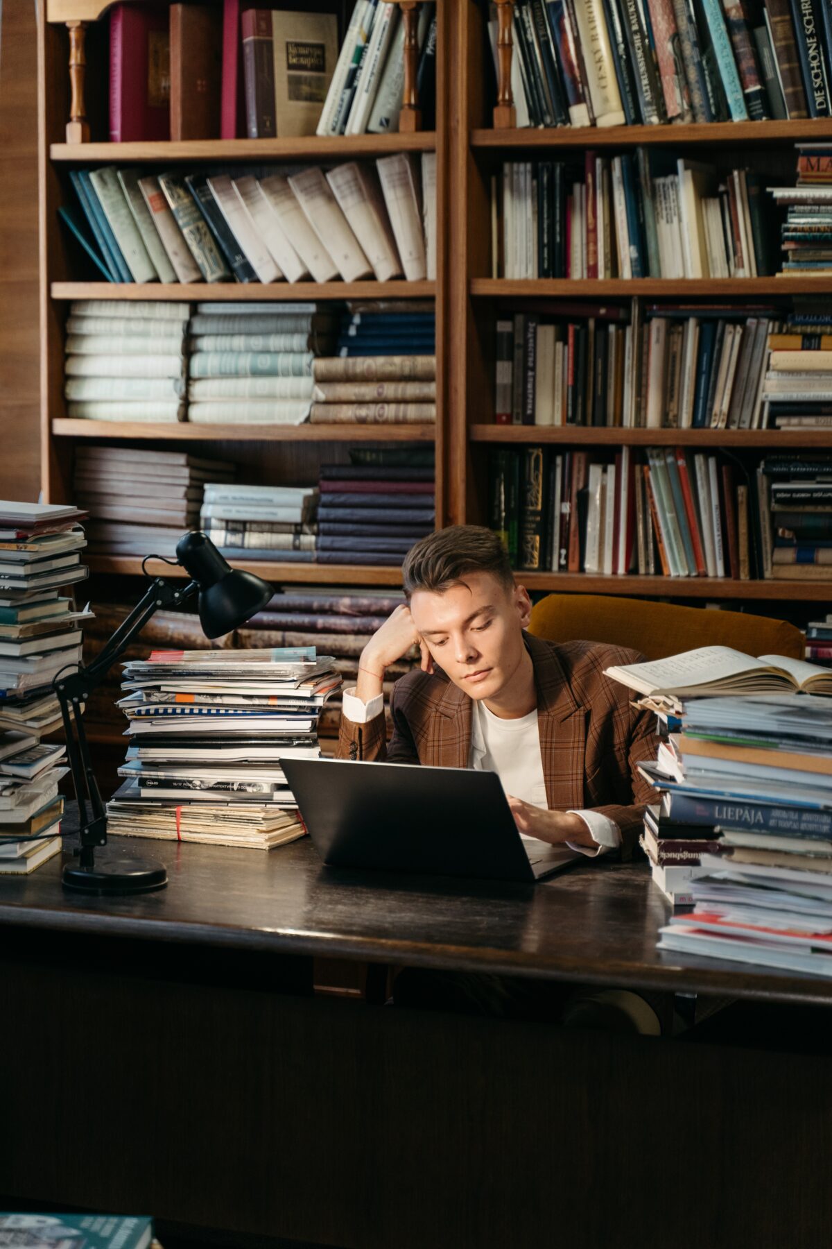 Man at a desk looking at his computer, and surrounded by books.