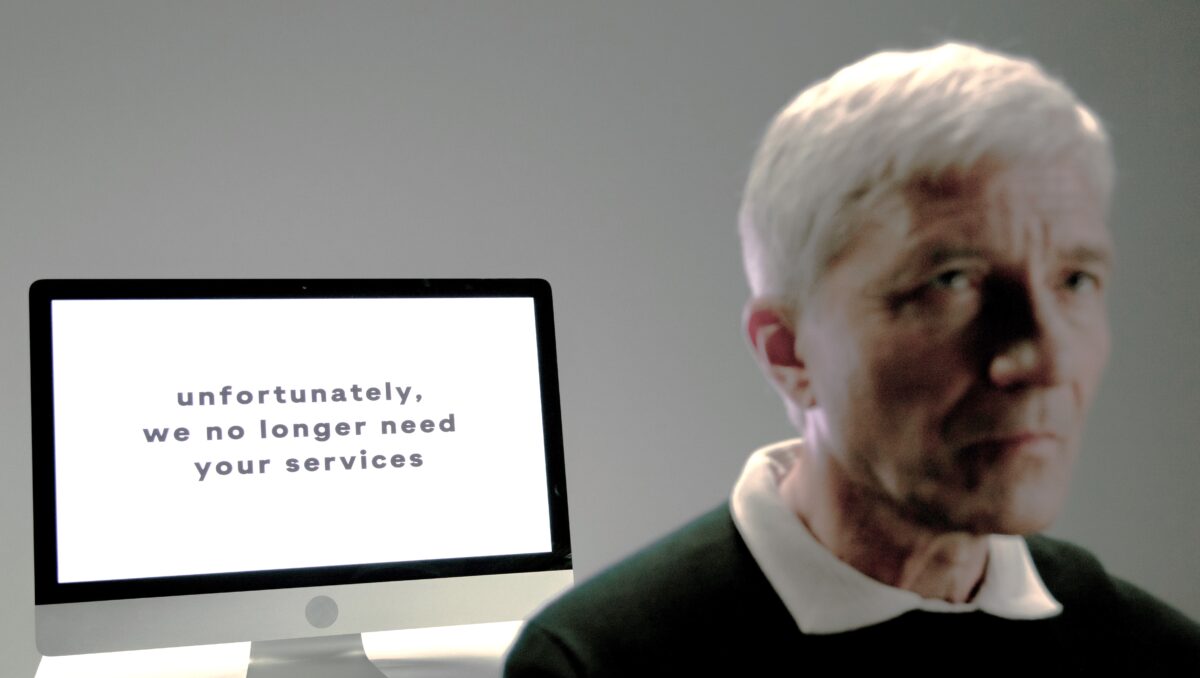 Man in front of computer screen which says that his services are no longer required.
