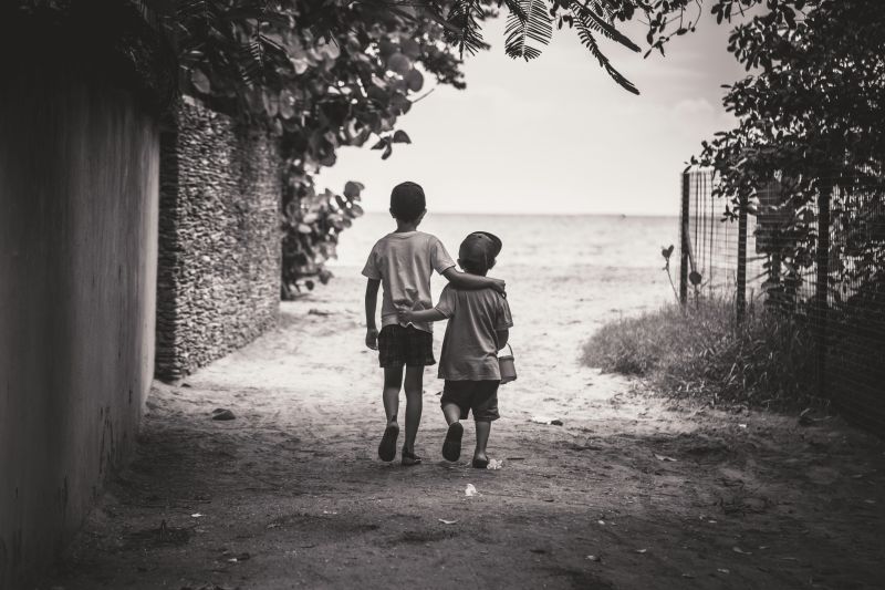 A young boy with his arm around a young girl, likely his sister, seen from the back and overlooking the water.