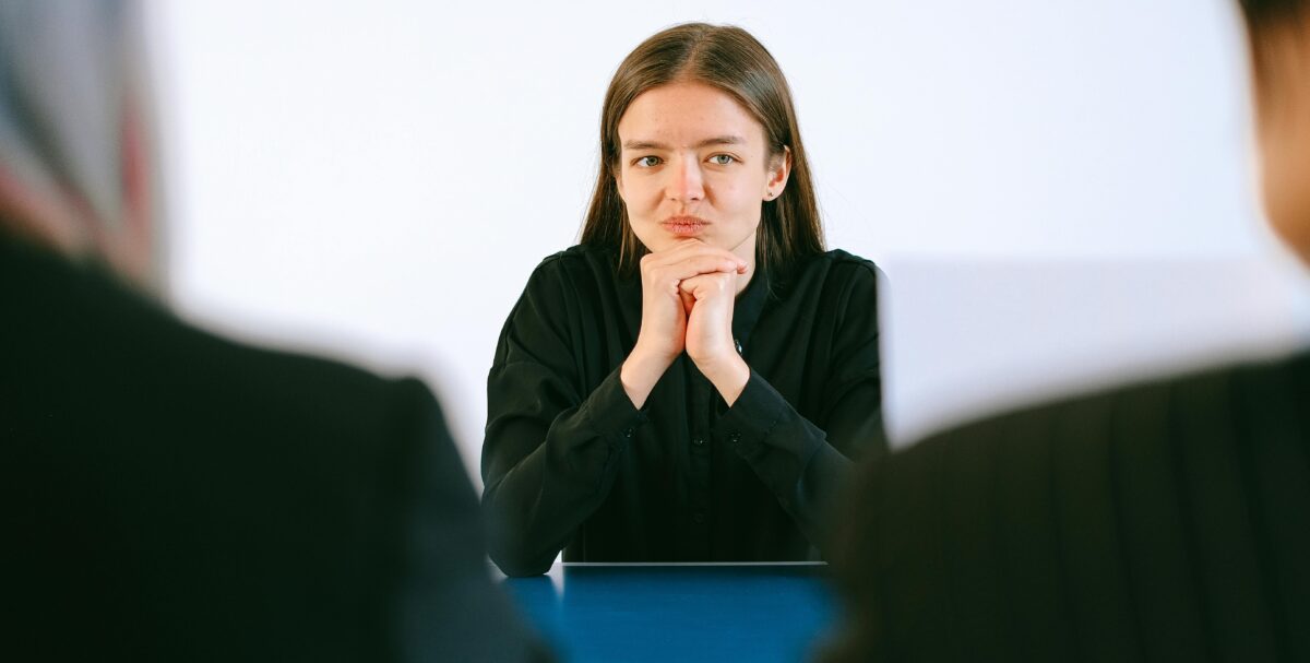 A woman facing two interviewers. Only her face is visible.