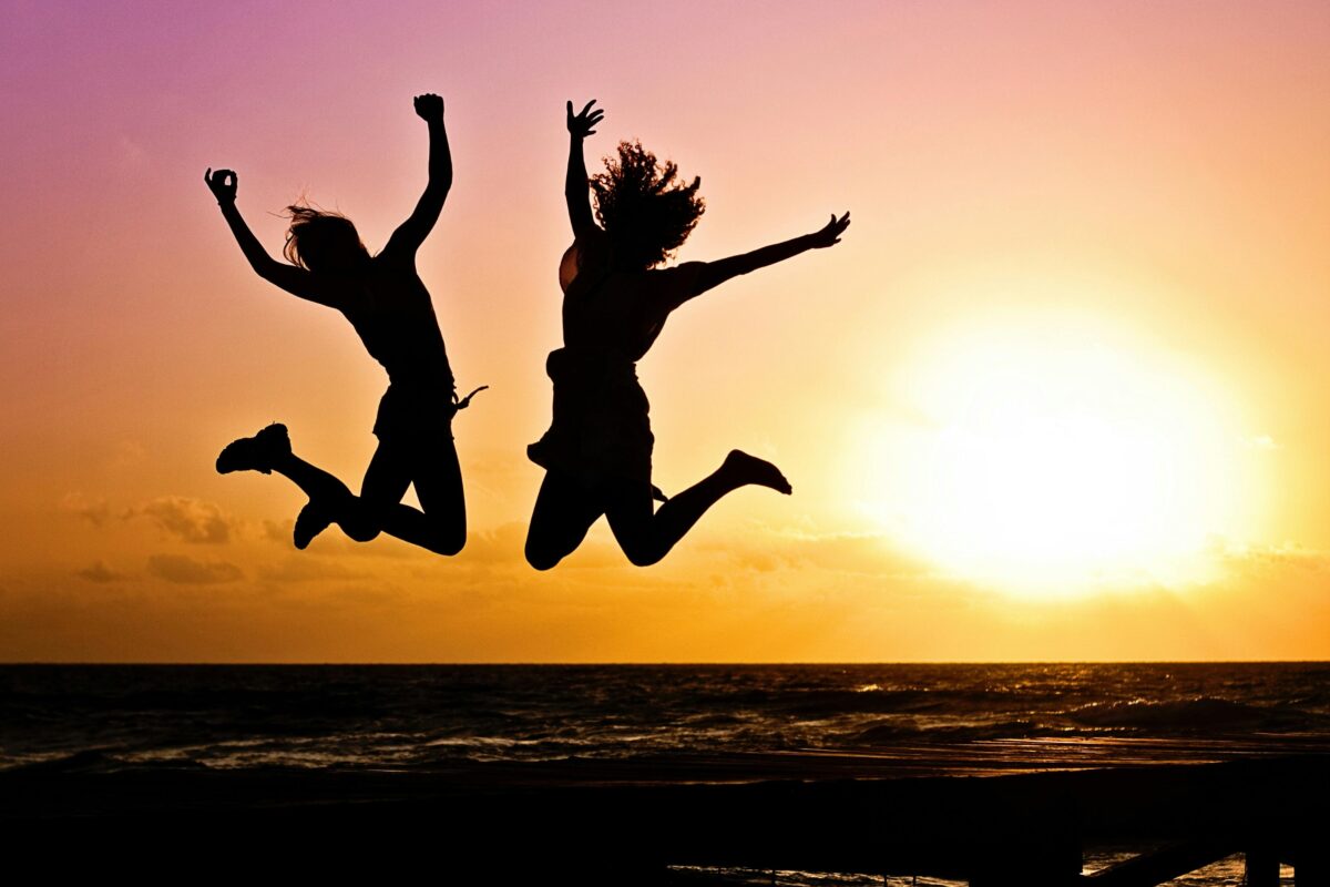 Two people jumping for joy against a background of the ocean and a sunset.