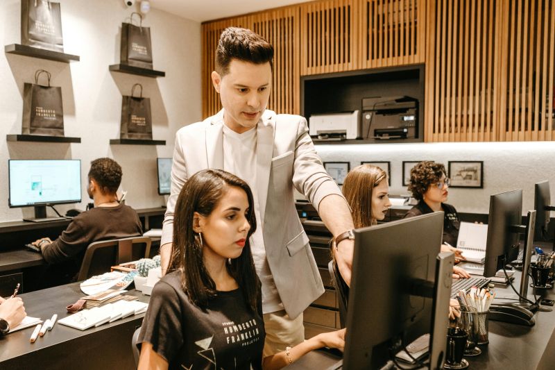A man instructing a woman who is working at a computer.