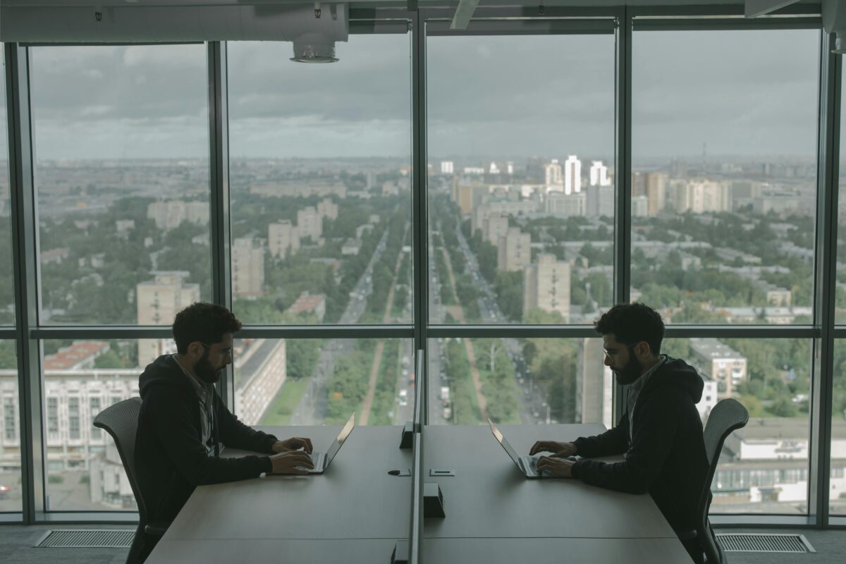 Twin men working on computers across from each other at a boardroom table.