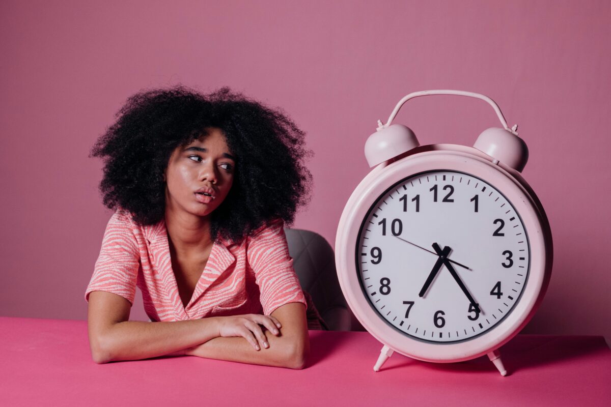 Frustrated woman looking at giant alarm clock.
