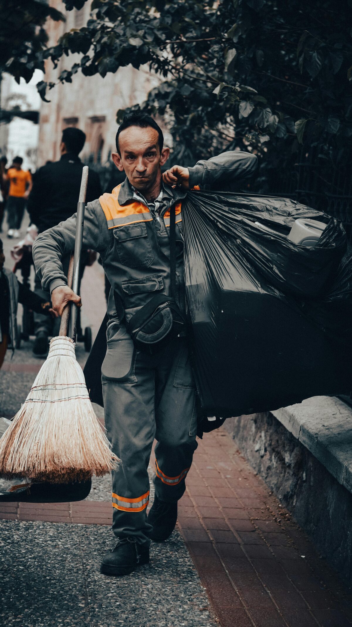 A man holding a broom and garbage bags.