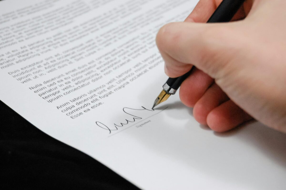 A hand holding a pen and signing a legal document.