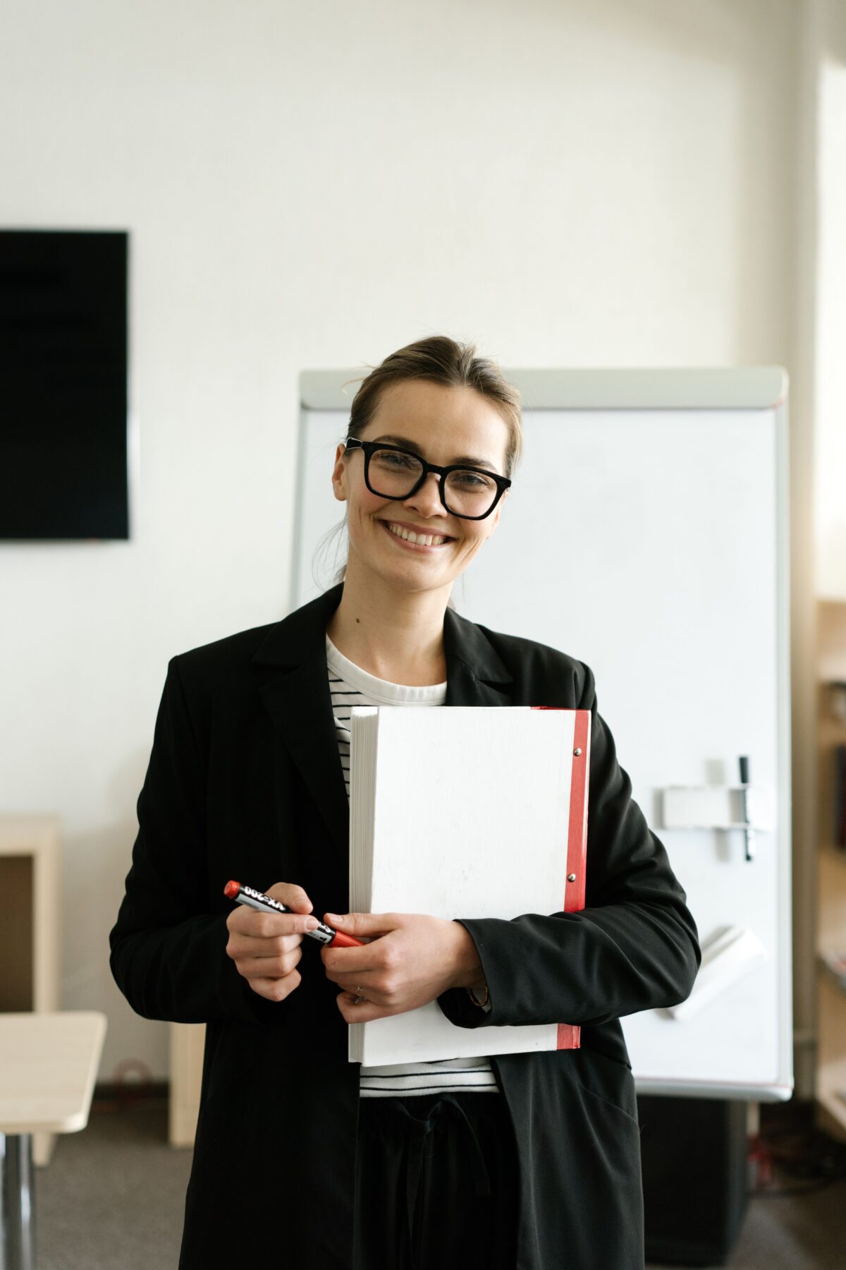 A woman holding a folder standing in front of a whiteboard.