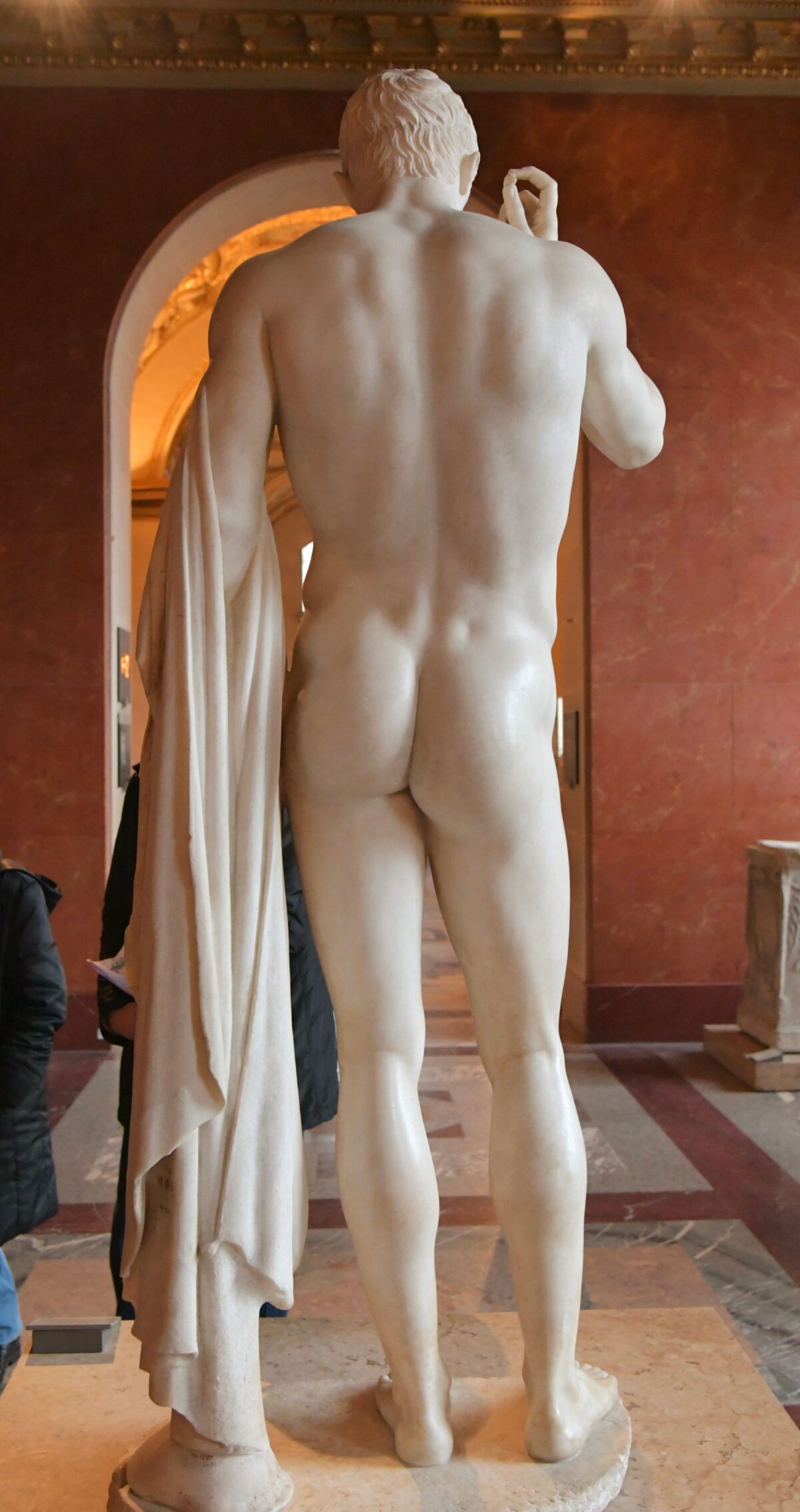 A statute for a Naked Man holding a robe seen from behind.