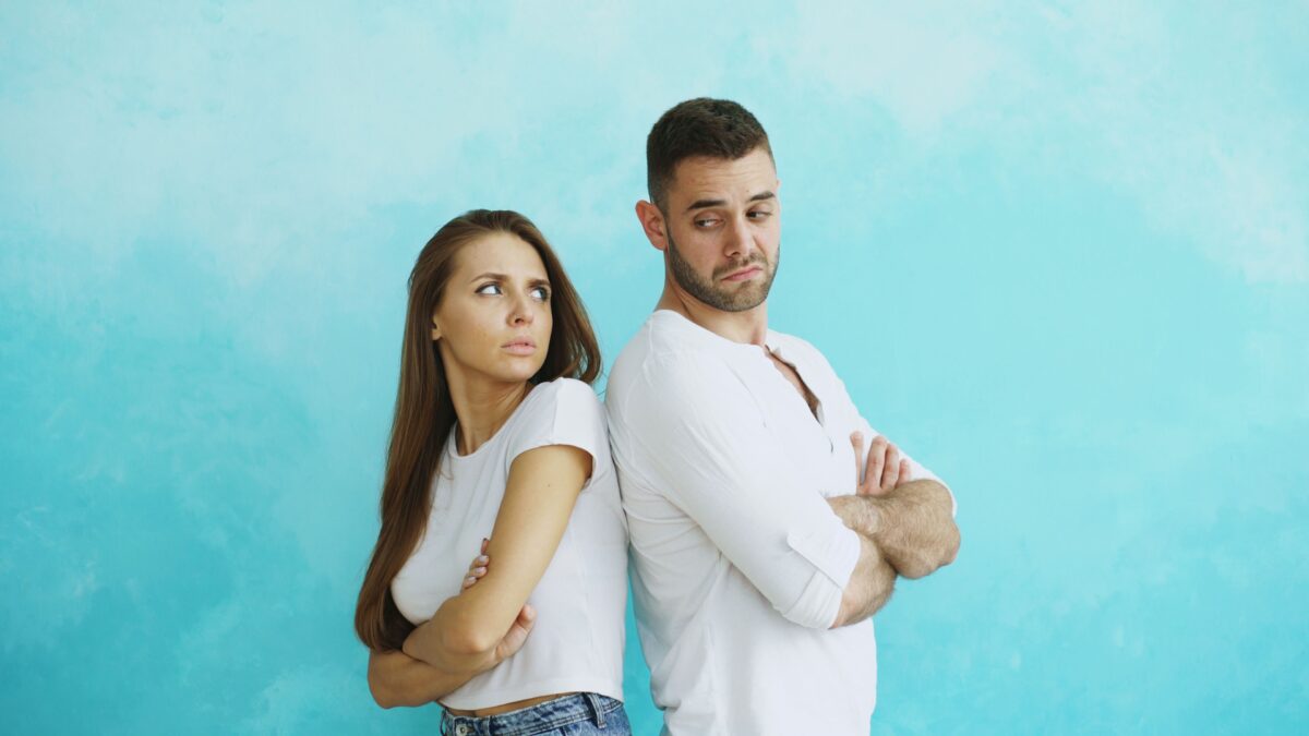 A man and a woman looking upset, standing back to back and looking over their shoulders at each other.